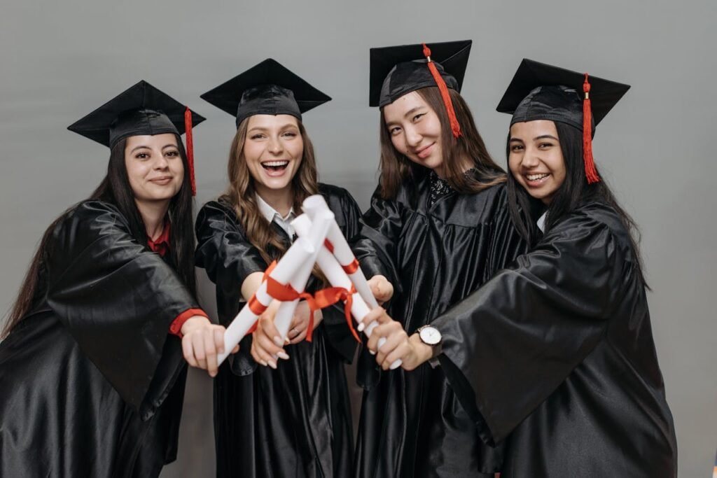 A joyful group of multiracial women in graduation gowns holding diplomas.